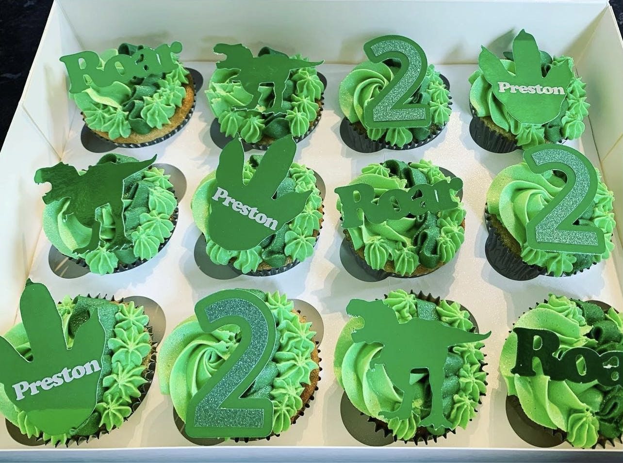 Green frosted cupcakes with dinosaur shapes on top for a second birthday