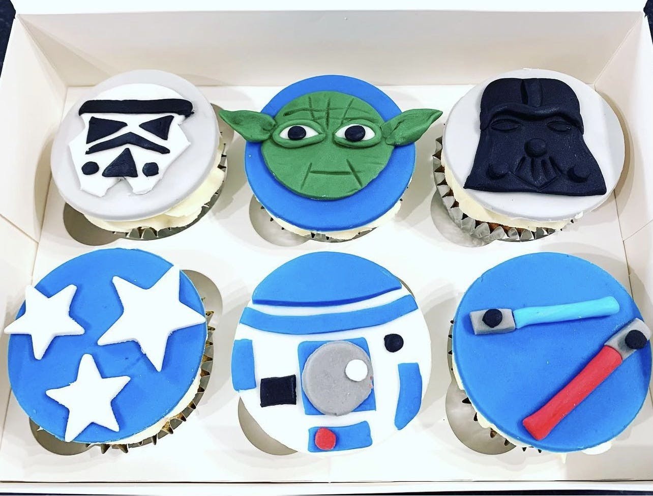 Blue and white cupcakes with a fondant storm trooper, yoda, darth vader, R2-D2 and lightsabers on top