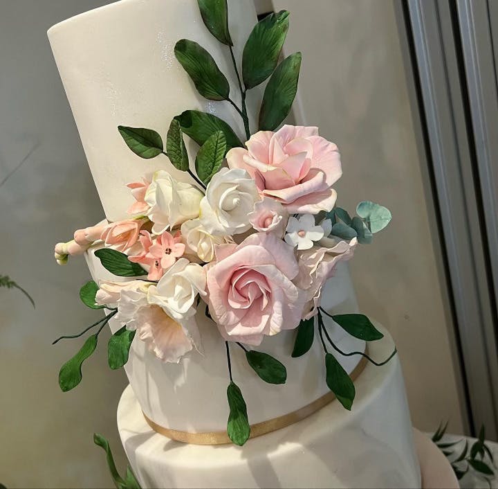 Close-up white wedding cake with fondant leaves and rose coloured flowers