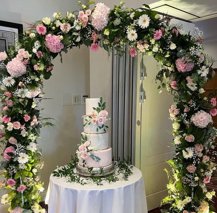 White wedding cake between an arch of leaves and flowers surrounded by a ring of leaves