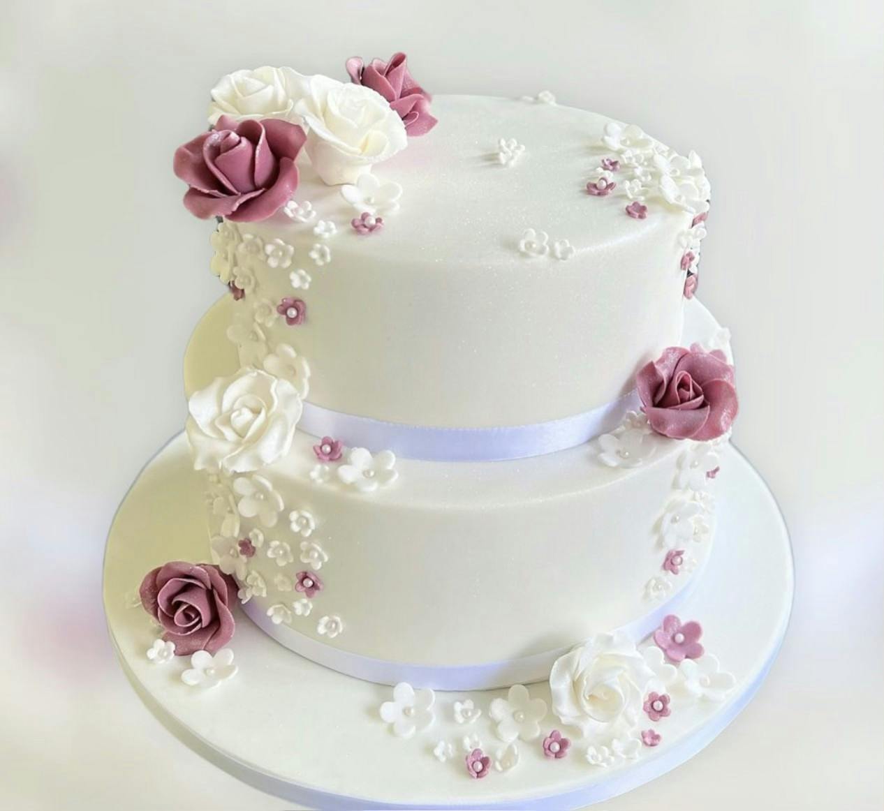 White wedding cake with white and purple flowers and silver ribbon