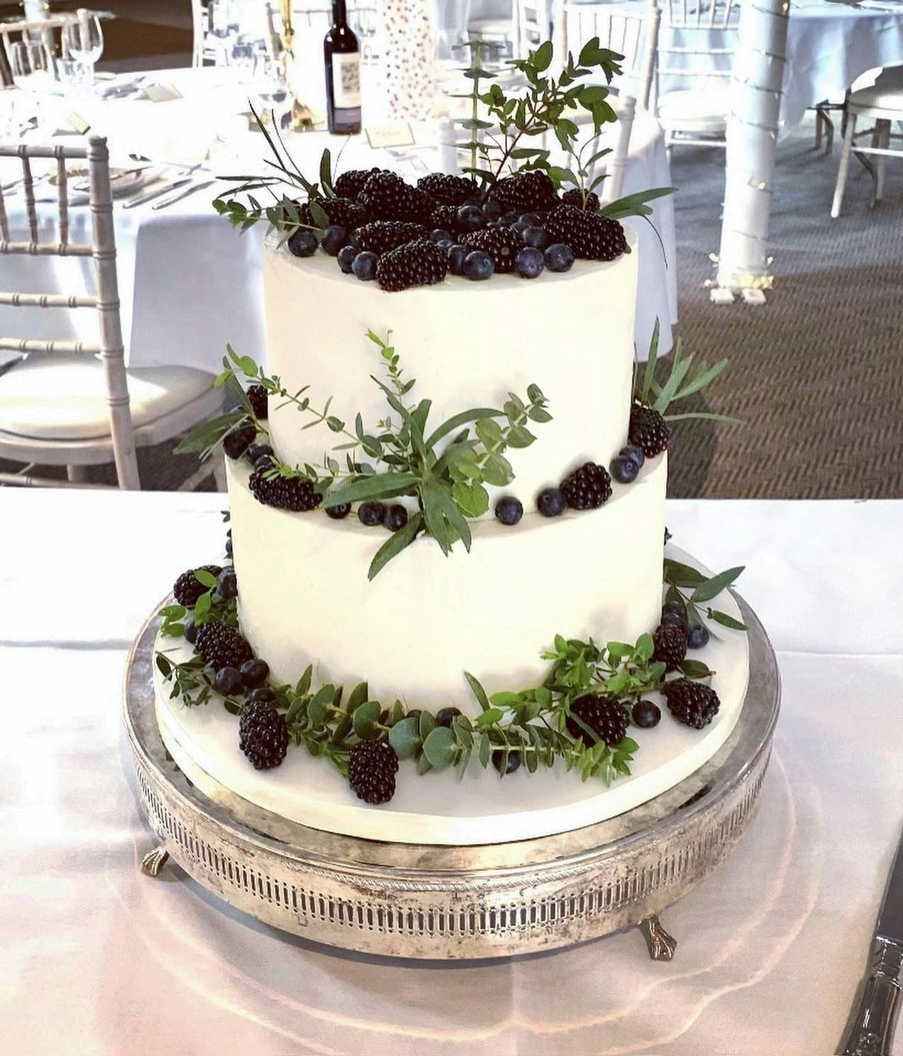 White natural wedding cake with blackberries, blueberries, foliage and a marble base