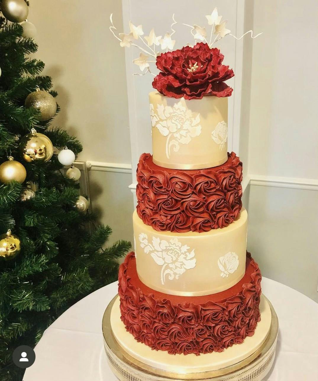 Red and pink wedding cake with swirly red icing flowers on alternating layers and a red rose on top