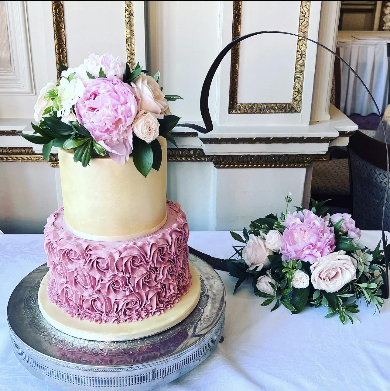White and rose coloured two-tiered wedding cake with flowers on top
