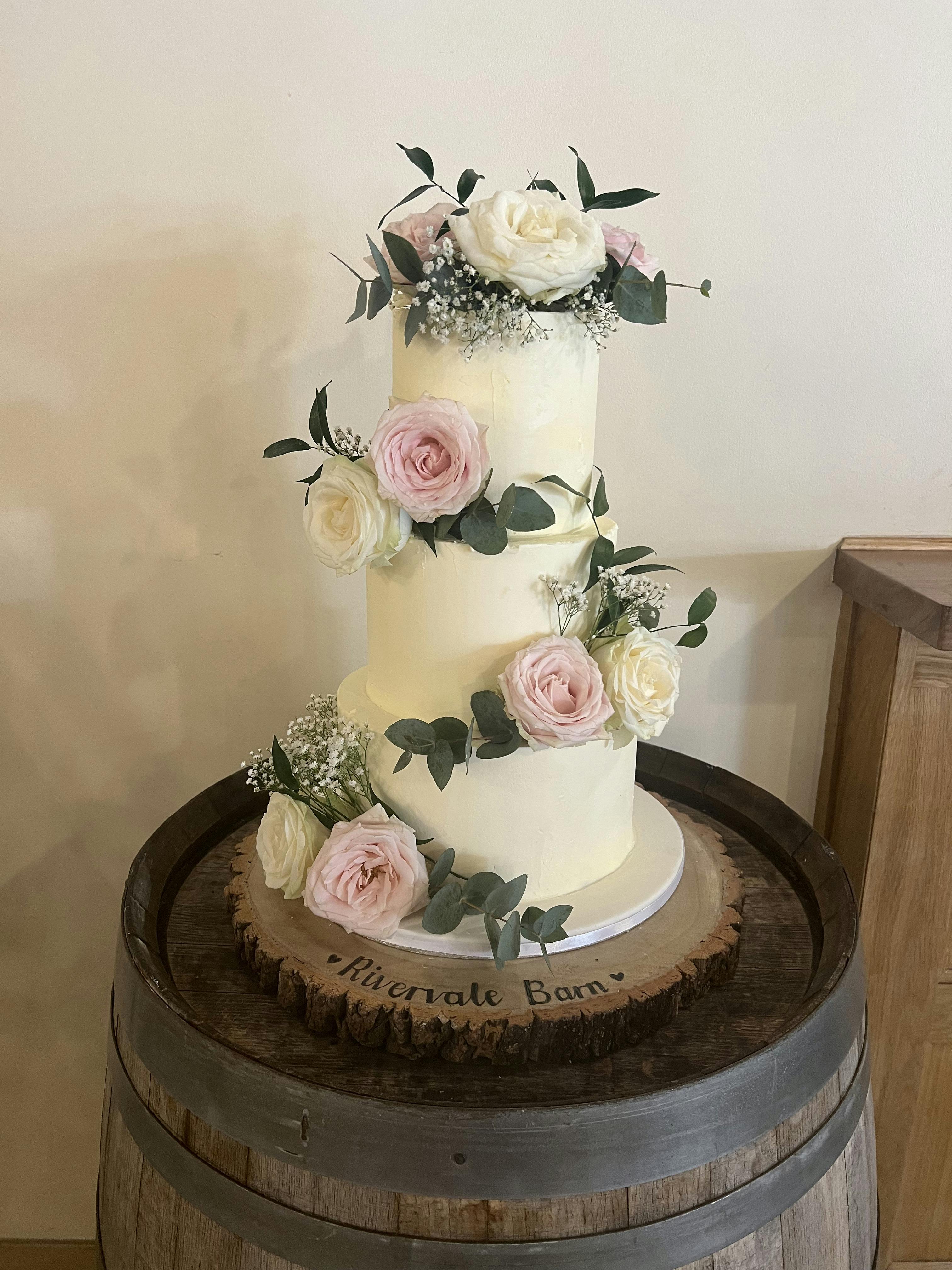 White wedding cake with leaves and flowers on top of a wooden barrel